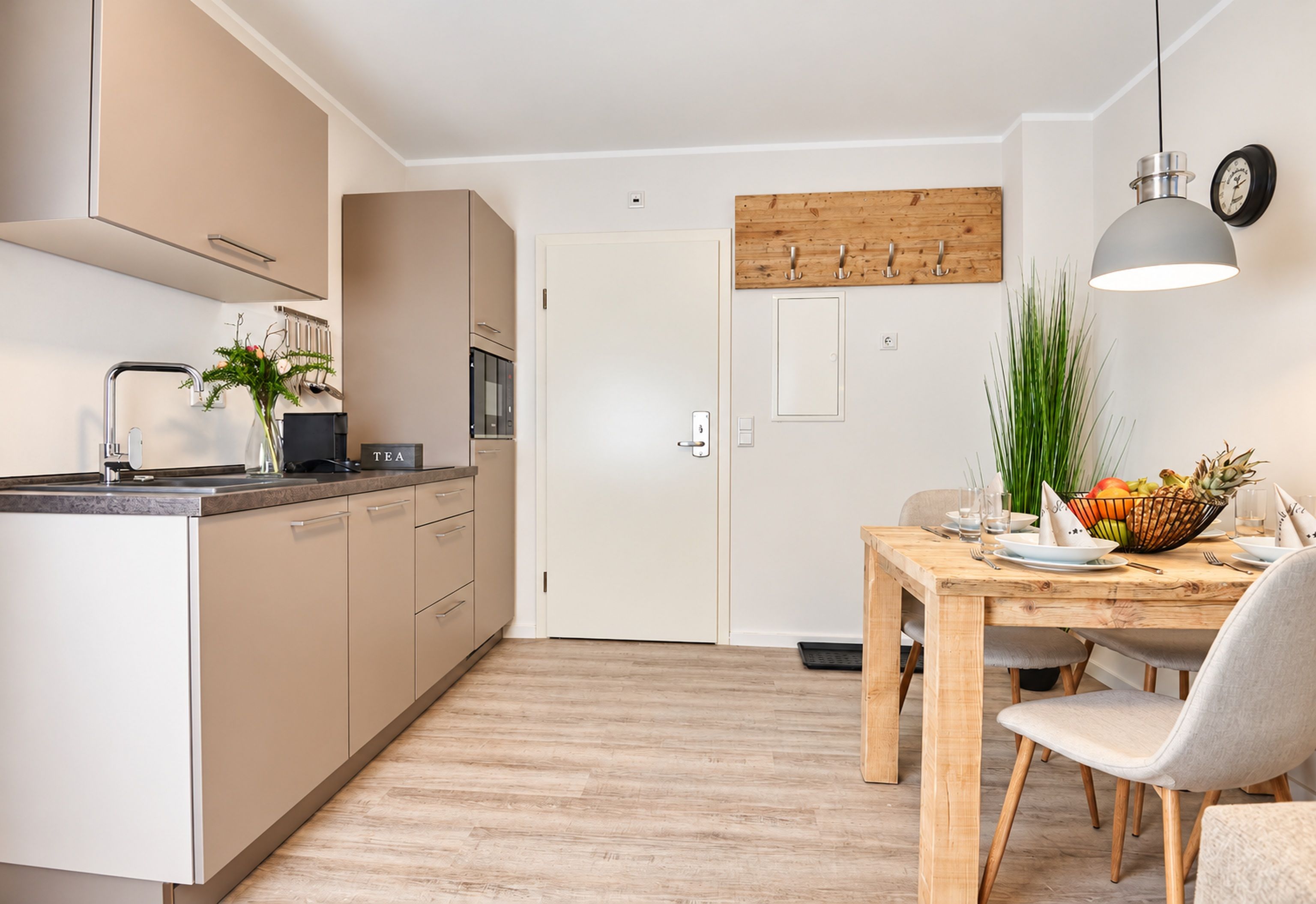 A modern kitchen with a dining area, featuring a wooden table, chairs, and a fruit bowl.
