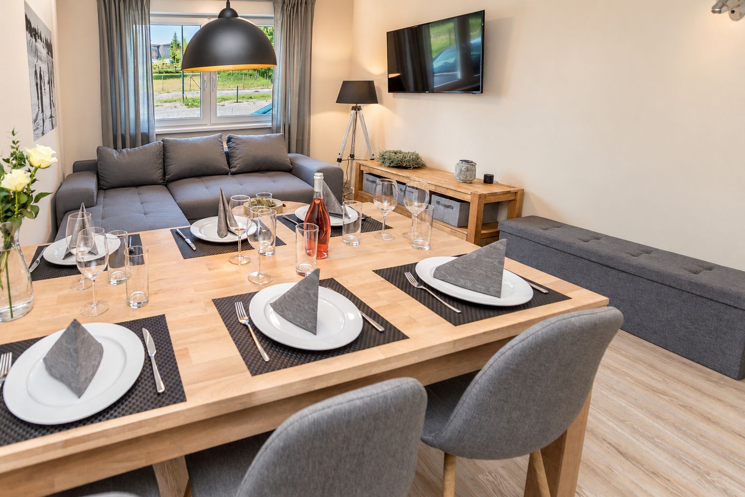 A dining area with a wooden table set for four, a sofa, and a TV mounted on the wall.
