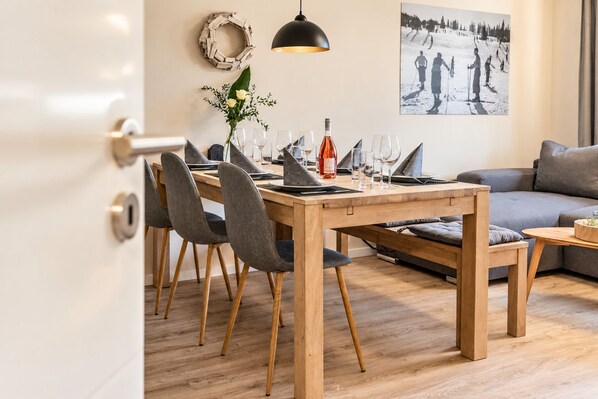A modern dining area with a wooden table, grey upholstered chairs, and a grey sofa.
