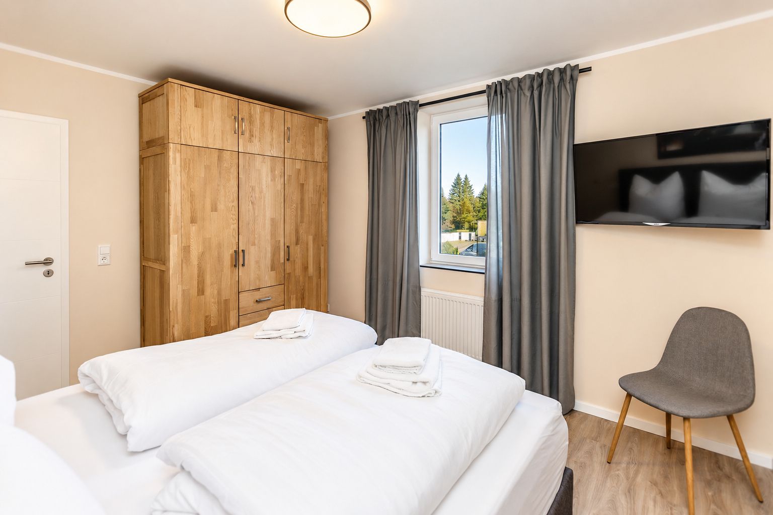 Une chambre d’hôtel avec deux lits, une armoire, une télévision et une fenêtre avec des rideaux.