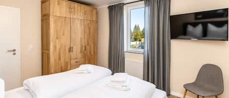 Een hotelkamer met twee bedden, een kledingkast, een televisie en een raam met gordijnen.