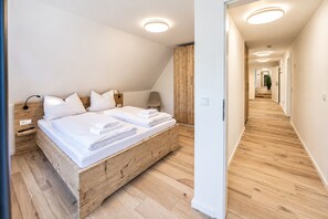 A modern bedroom with a wooden bed frame, white bedding, and a bedside lamp.