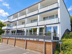 Un hôtel à plusieurs étages doté de balcons, d’un espace extérieur couvert aménagé en coin salon et d’un parking.