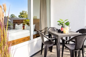 An outdoor dining area with wicker furniture, a table with a potted plant, and a view of a garden through a glass door.