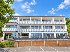 Un immeuble à plusieurs étages doté de balcons, de grandes fenêtres et d’un espace de stationnement.