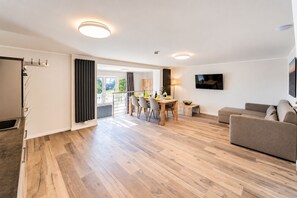 A modern living room with a sofa, a dining area with chairs, and a TV mounted on the wall. - Smart Resorts - Haus Diamant - Ferienwohnung 706 mit Balkon, Max. 6 Personen (Winterberg)