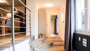 A modern interior with a staircase leading to a second floor, a wooden floor, a radiator, and a window with curtains.