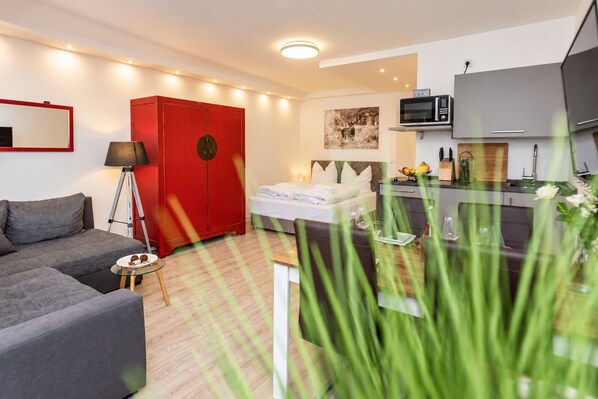 Een moderne hotelkamer met een bed, een rode garderobe, een kitchenette en een grijze bank.