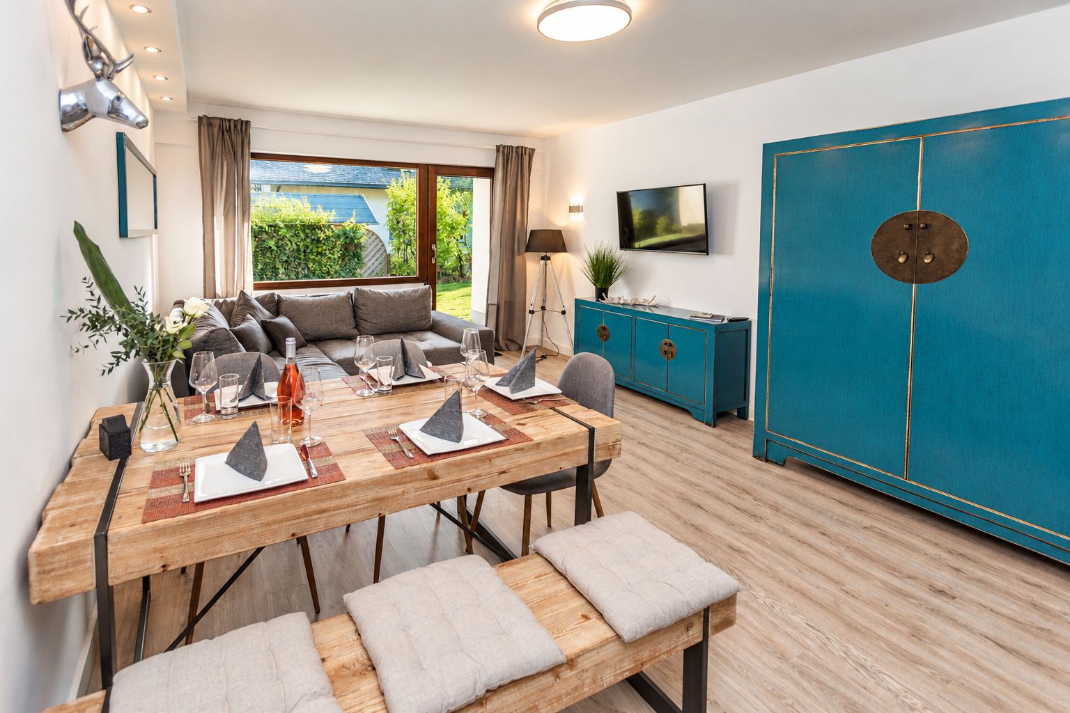 Un salon moderne comprenant un coin repas, un ensemble de canapés, un téléviseur et un grand meuble bleu.