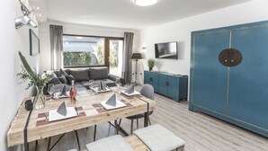 A modern living room with a wooden dining table set for four, a sofa, a blue cabinet, and a TV mounted on the wall. - "Charming Getaway in Winterberg: Your Perfect Family Retreat Awaits!" (Winterberg)
