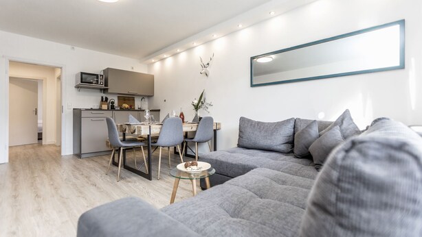 A modern living room with a grey sofa, a dining table with chairs, a kitchen area with a microwave, and a large mirror on the wall. - "Charming Getaway in Winterberg: Your Perfect Family Retreat Awaits!" (Winterberg)