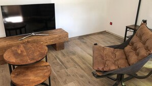A modern living room with a wooden coffee table, a TV on a stand, a brown cushioned chair, and a small table with a remote control.