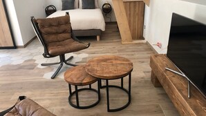 A modern bedroom with a bed, a wooden TV stand, a brown leather chair, and two round tables.