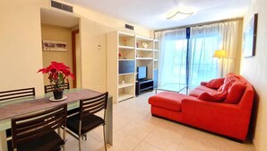 Un salon avec un canapé rouge, une table à manger avec des chaises, un téléviseur et une bibliothèque.