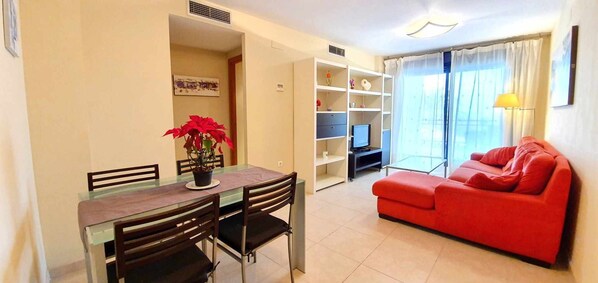A living room with a red sofa, a dining table with chairs, a TV, and a bookshelf.