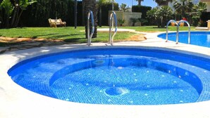 Une piscine avec deux escaliers menant à l’intérieur, entourée d’une pelouse et de palmiers.
