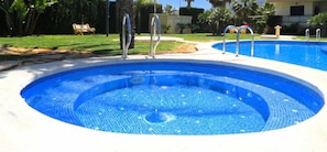 A swimming pool with two sets of stairs leading into it, surrounded by a grassy area and palm trees.