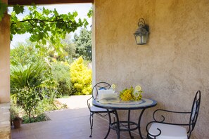 Une terrasse extérieure avec une table ronde, deux chaises, un pot de fleurs et une lanterne fixée au mur.