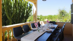 Un espace de restauration en plein air avec une table dressée pour quatre personnes, entourée de chaises, et offrant une vue sur un grand cactus et une végétation luxuriante en arrière-plan.