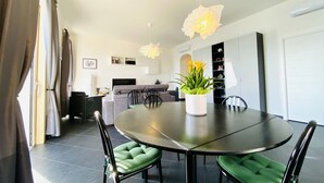 Un espace repas moderne avec une table ronde, des chaises recouvertes d’un tissu vert et une plante en pot.