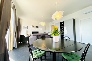 A modern dining area with a round table, green upholstered chairs, and a potted plant.