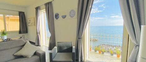 Un balcón con vistas al mar, un sofá, una silla y plantas en macetas.