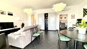 Un salon moderne comprenant un canapé, des fauteuils, un téléviseur et un coin repas avec une table et des chaises.