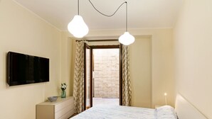 Een slaapkamer met een bed, een dressoir, een televisie en uitzicht op een stenen muur door een deuropening.