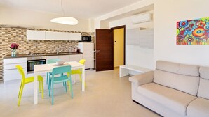 Een moderne keuken met witte kastjes, een magnetron, en een eetgedeelte met een witte tafel en kleurrijke stoelen.