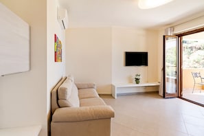 Un salon moderne avec un canapé beige, un téléviseur à écran plat fixé au mur, un banc et une porte-fenêtre coulissante donnant sur un espace extérieur.