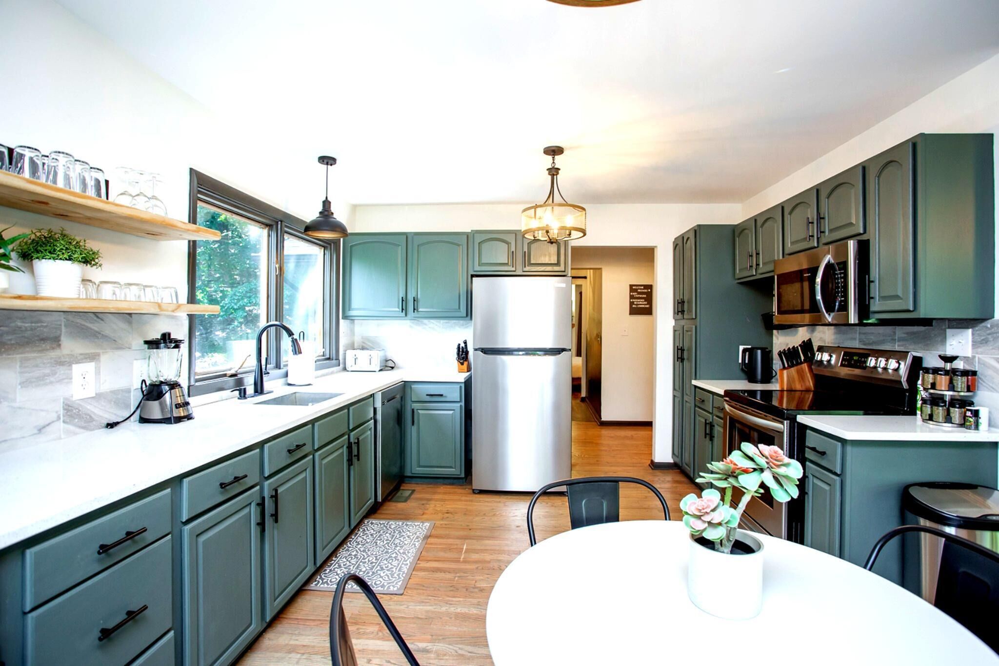 A modern kitchen with green cabinets, stainless steel appliances, and a dining area with a white table and chairs.