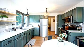 A modern kitchen with green cabinets, stainless steel appliances, and a dining area with a white table and chairs.