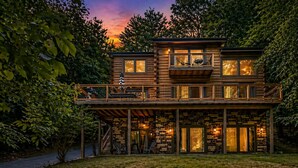 Eine zweistöckige Blockhütte mit Balkon, Steinunterbau und Blick auf den Sonnenuntergang.