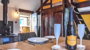 A dining table with a bottle of Prosecco, two wine glasses, and a wooden cutting board.