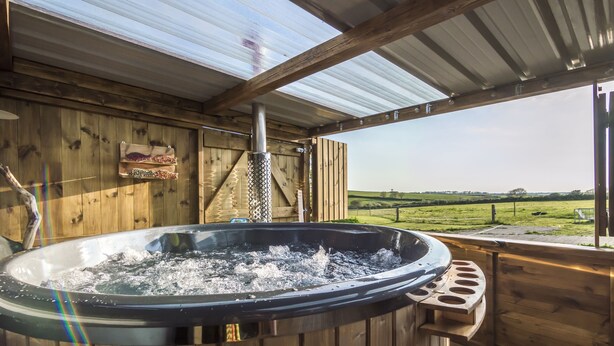 A hot tub in a wooden deck area with a view of a grassy field.