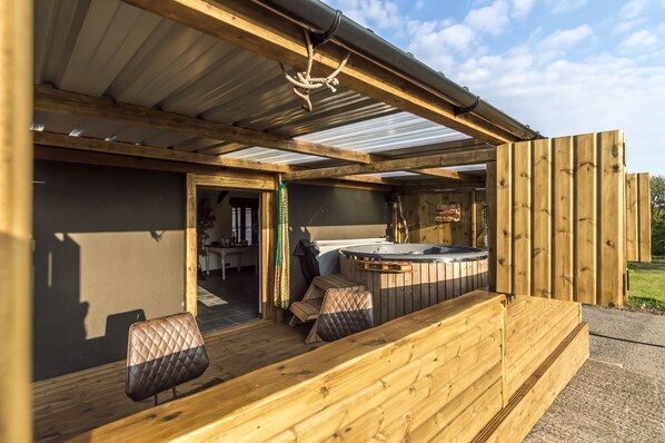 Una terraza de madera con jacuzzi, asientos y vistas al exterior.