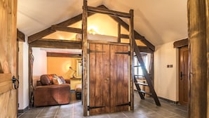 A loft-style bedroom with a wooden ceiling, a loft bed, a brown leather sofa, and a wooden door.