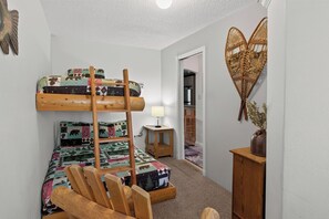 A bunk bed with a ladder, a bedside table with a lamp, and a decorative wall piece.