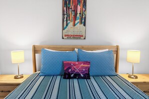 A hotel room with a bed, two bedside lamps, a wall-mounted poster, and a striped bedspread.