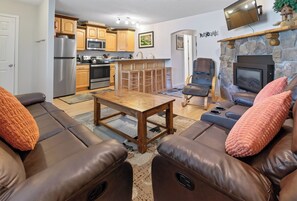 A living room with a brown leather sofa, a wooden coffee table, and a stone fireplace. - Right on Main Street Amazing Views of the Ski Area (Breckenridge)