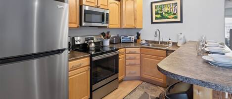 A modern kitchen with stainless steel appliances, wooden cabinets, a microwave, a toaster, and a sink.