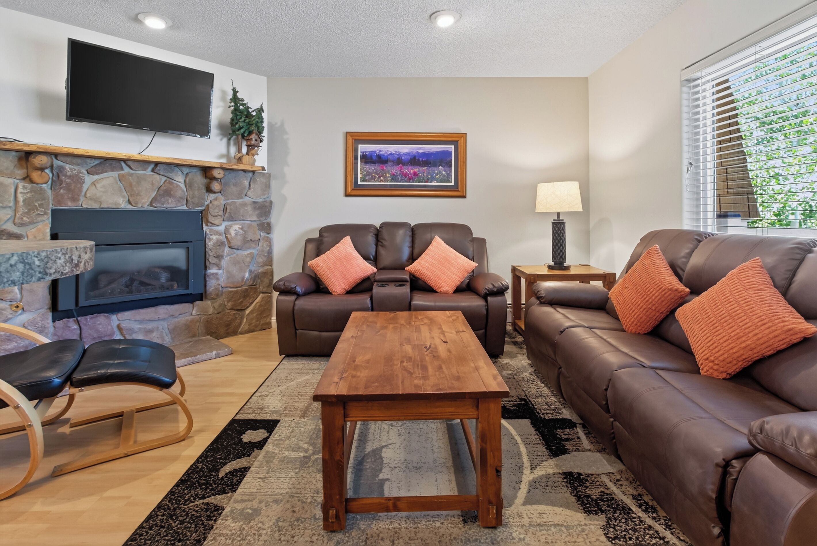 A living room with a stone fireplace, leather sofas, a wooden coffee table, and a flat-screen TV mounted on the wall.