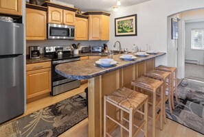 A kitchen with wooden cabinets, stainless steel appliances, a granite countertop, and a bar area with stools.