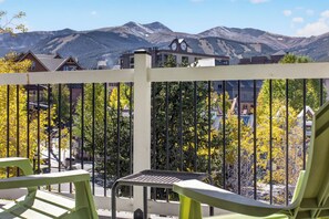 A balcony with a view of mountains, a white fence, and green chairs.