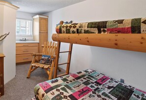 A bunk bed with a quilt, a wooden chair with a cushion, a desk, and a window with blinds. - Right on Main Street Amazing Views of the Ski Area (Breckenridge)