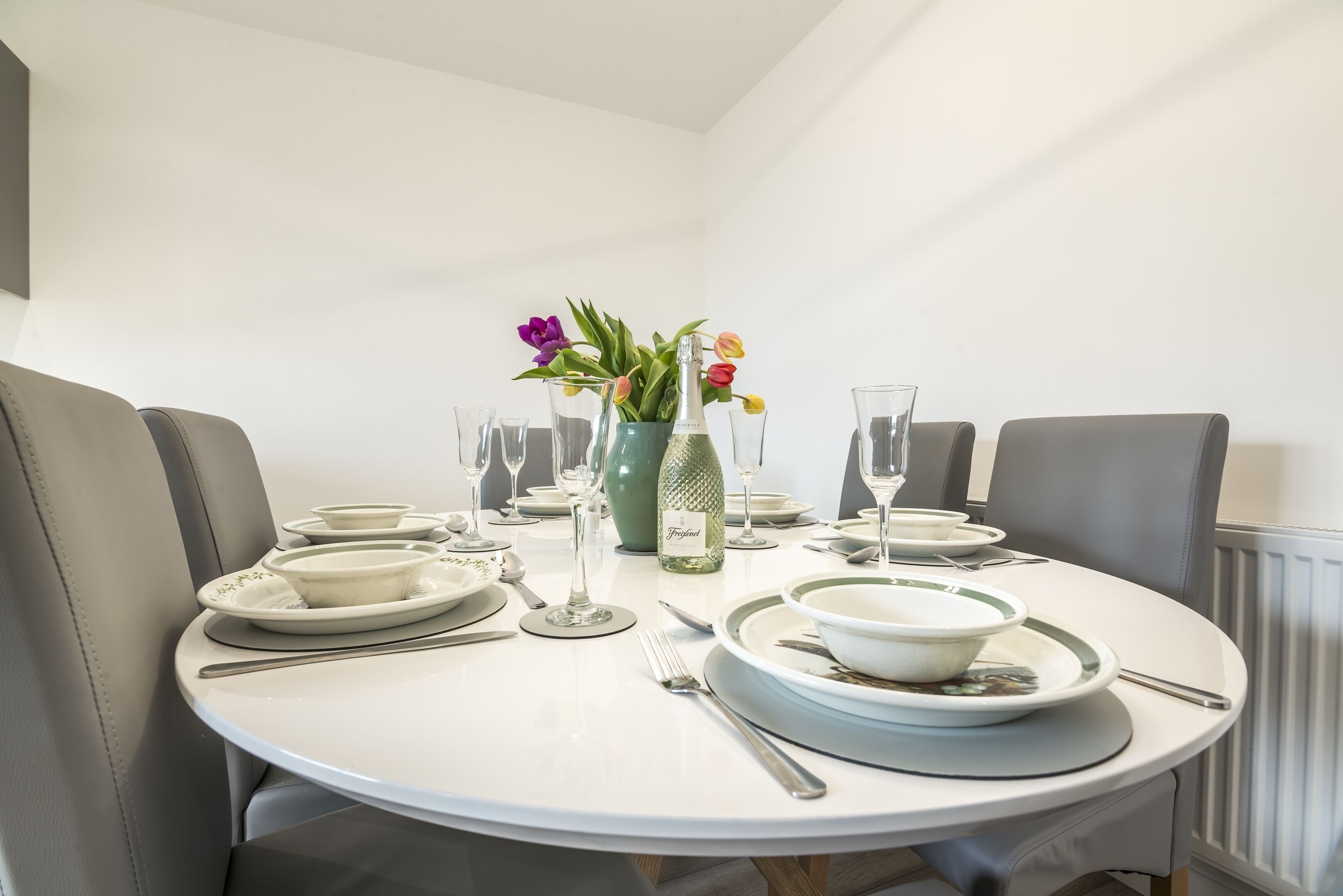 A round dining table with white plates, bowls, and cutlery, set for a meal.