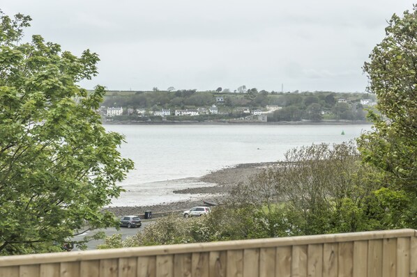 A coastal view with a wooden deck, a rocky shoreline, and buildings in the background. - Martello View - 3 Bedroom - Llanreath (Pembroke Dock)
