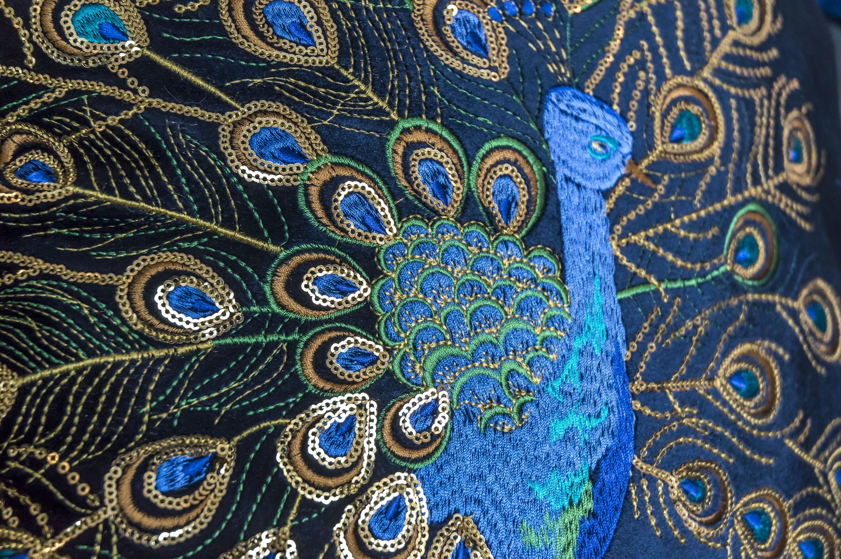 A close-up of a fabric with intricate peacock feather embroidery.
