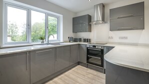 A modern kitchen with grey cabinets, a large window, and built-in appliances. - Martello View - 3 Bedroom - Llanreath (Pembroke Dock)