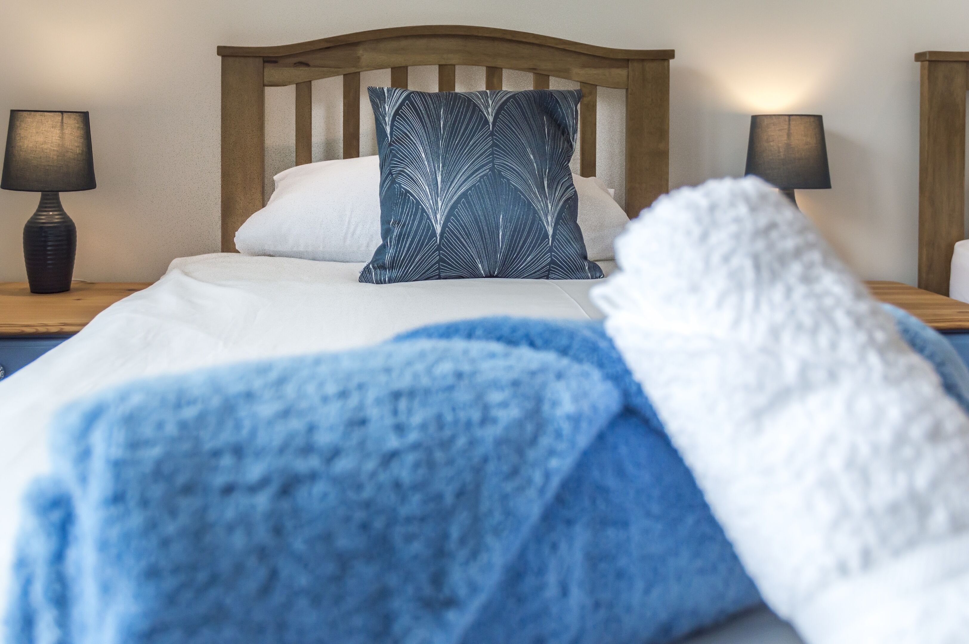A neatly made bed with a blue blanket and a decorative pillow, flanked by two bedside lamps on wooden nightstands.